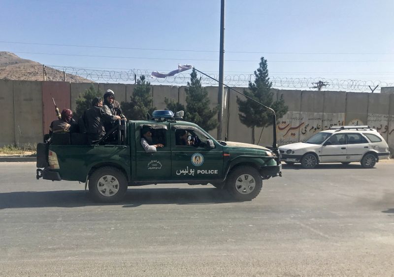 Taliban fighters ride on a police vehicle in Kabul
