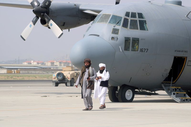 Taliban walk in front of a military airplane a day