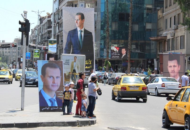 FILE PHOTO: People stand near posters depicting Syria’s President Bashar