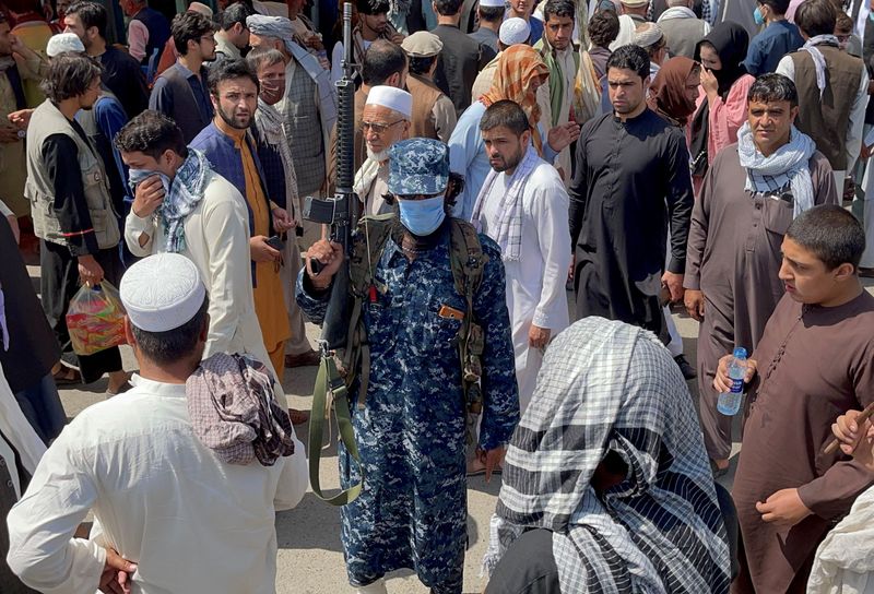 Member of Taliban security forces stands guard among crowds of
