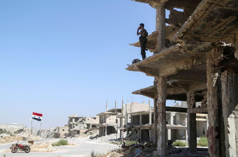 A Syrian army soldier stands on a damaged building in