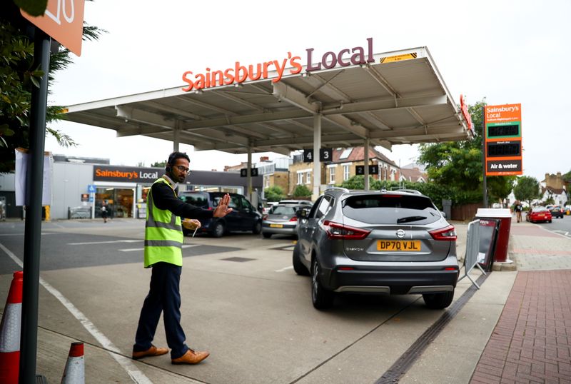 A worker guides vehicles into the forecourt as they queue