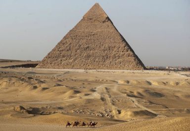 Tourists ride camels in front of the Great Pyramids of