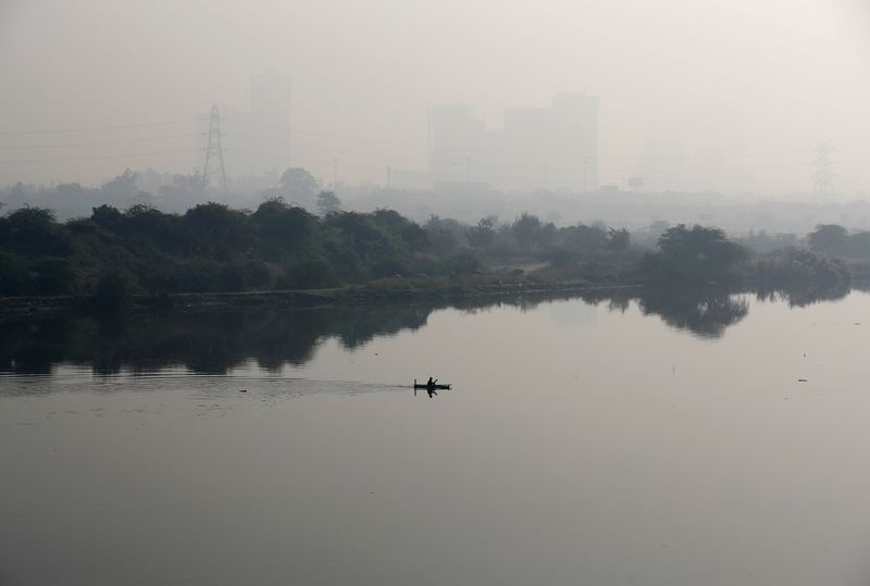 A man rows a boat as buildings shrouded in smog
