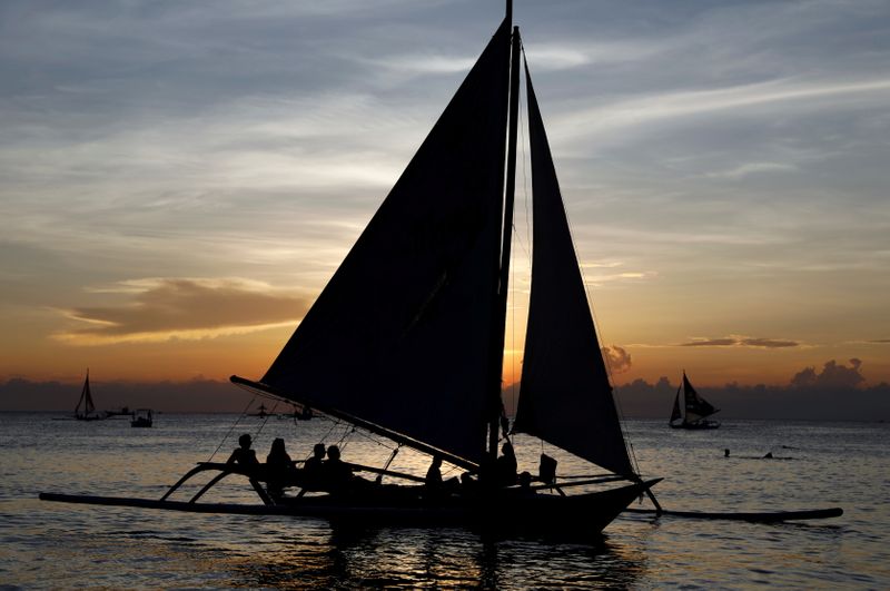 FILE PHOTO: Tourists watch sunset aboard sailboats, one day before