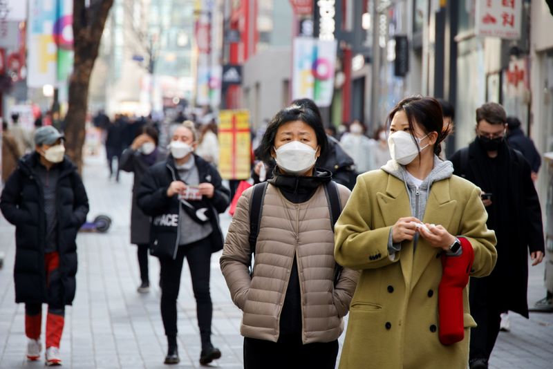 Women wearing masks walk in a shopping district amid the