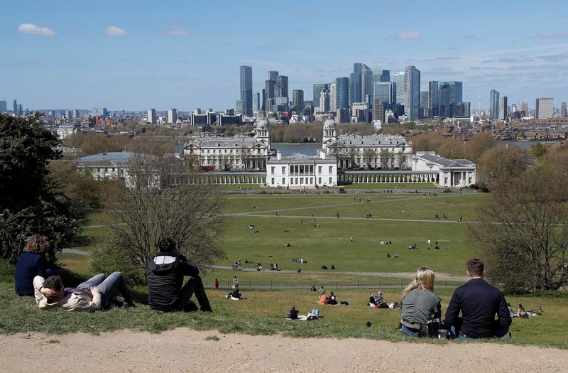 Visitors to Greenwich Park sit and look towards Canary Wharf
