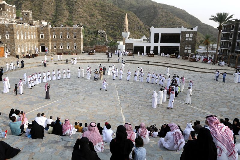 Tourists watch Saudi men perform a traditional folk dance at