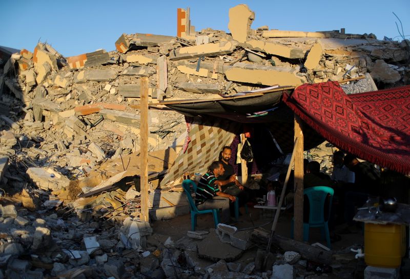 People sit near the rubble of their houses which were