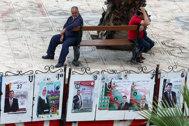 Men sit near parliamentary election campaign posters in Algiers