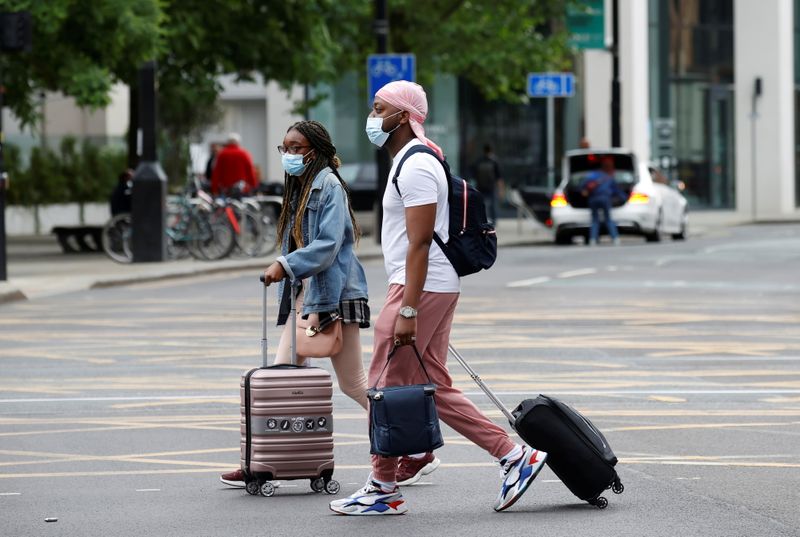 People wear protective masks as they walk with suitcases through