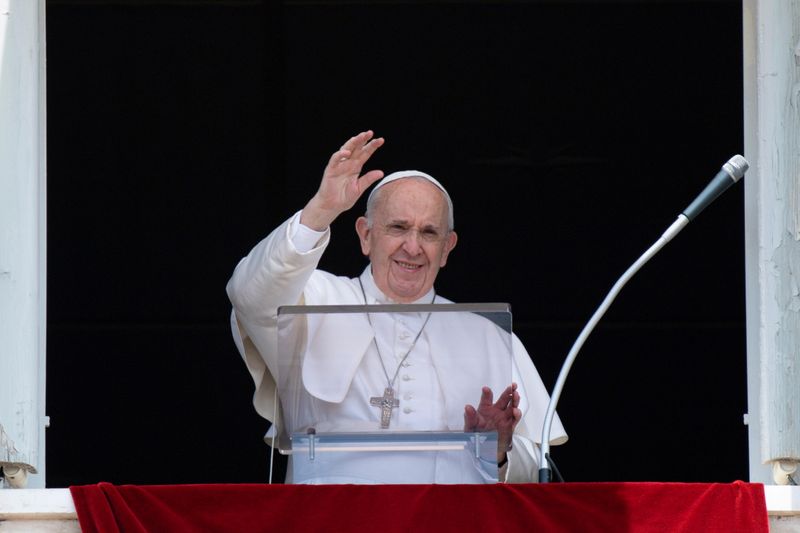 Pope Francis raises his hand in greeting as he delivers