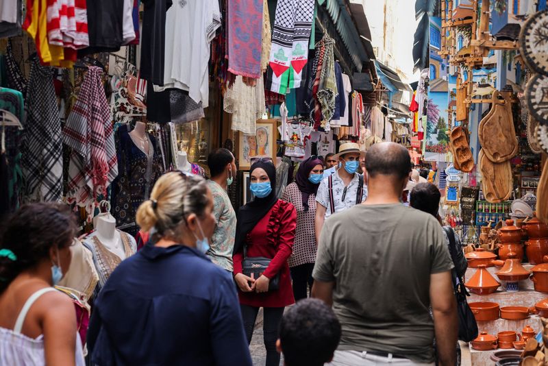 People wearing protective face masks walk past shops, amid the