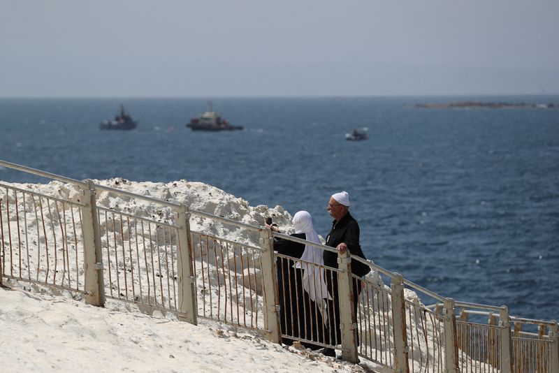 FILE PHOTO: People walk as Israeli navy boats are seen