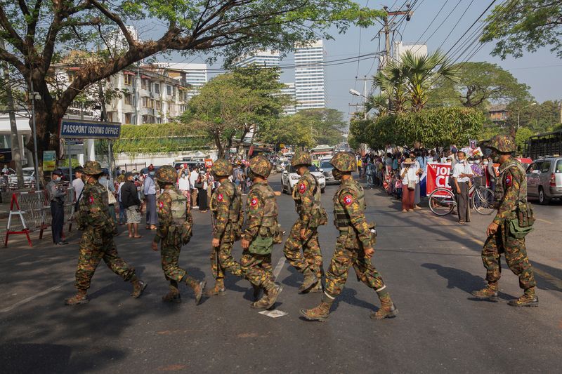 Soldiers cross a street as people gather to protest against