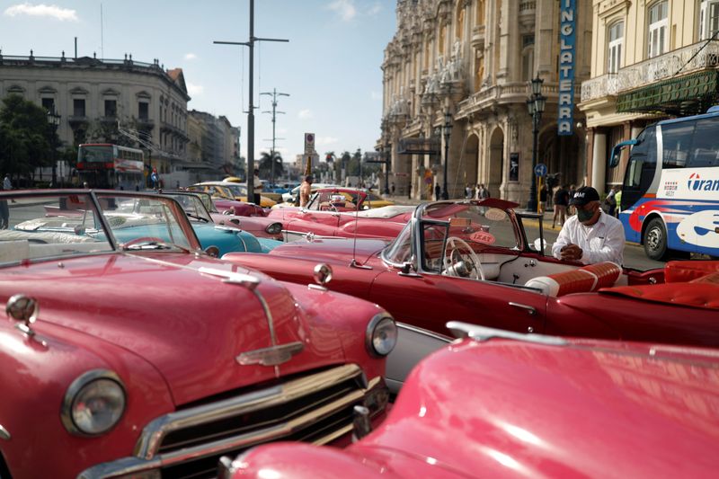 Taxi drivers wait for tourists next to vintage cars in