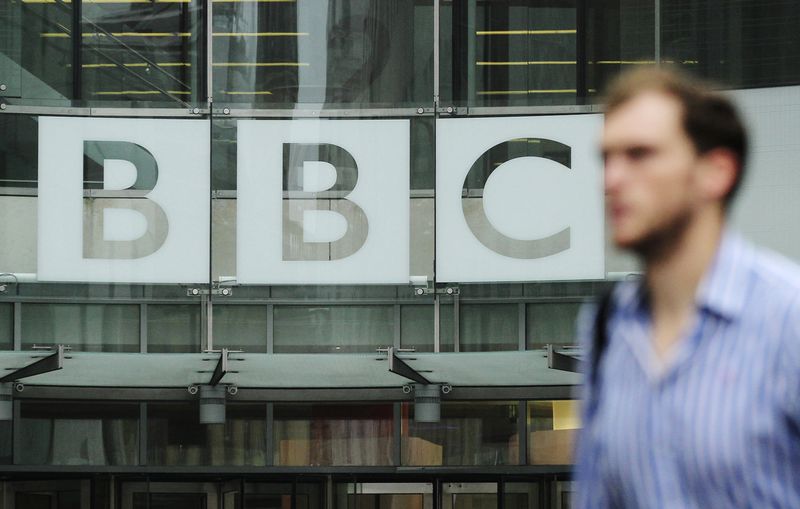 A pedestrian walks past a BBC logo at Broadcasting House