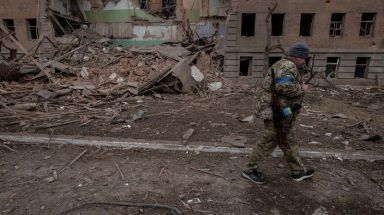 A Ukrainian service member walks past a destroyed building in
