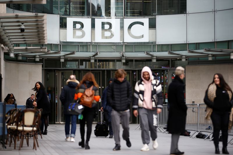 Pedestrians walk past a BBC logo at Broadcasting House, as