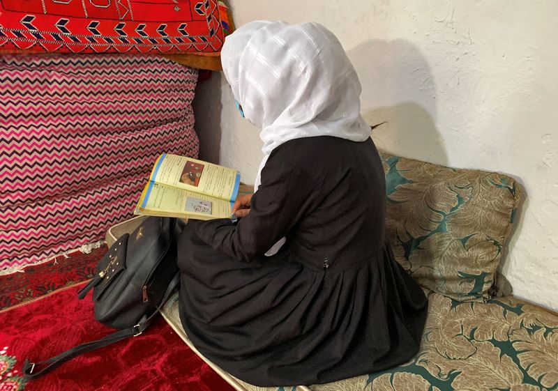 An Afghan schoolgirl reads from her book inside a house