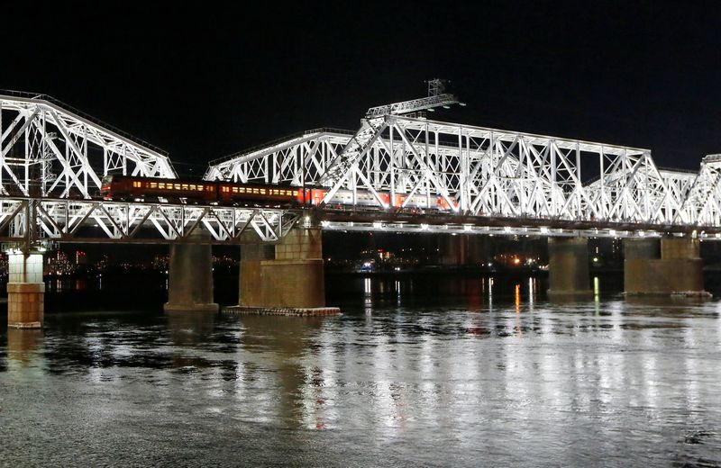 A passenger train moves along an illuminated bridge across the