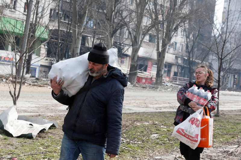 Local residents carry foodstuff while walking past a damaged apartment