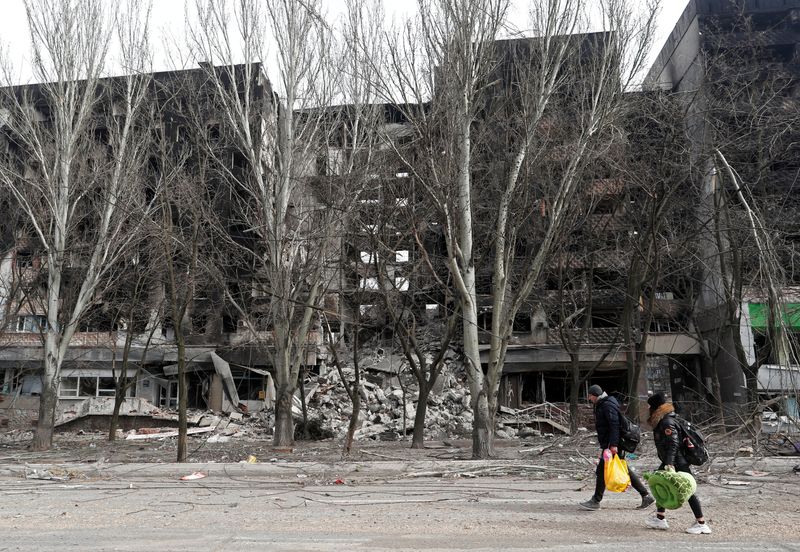 Local residents walk past a destroyed apartment building in Mariupol