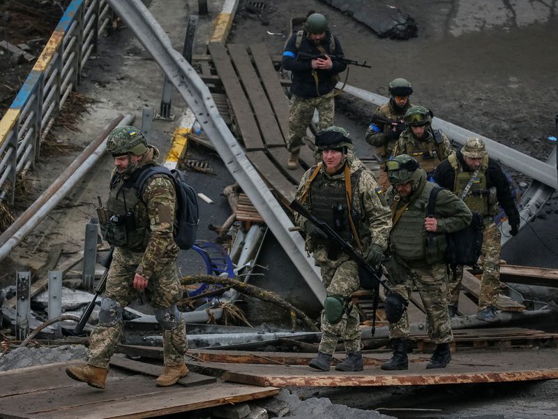Ukrainian servicemen walk on a destroyed bridge in the town