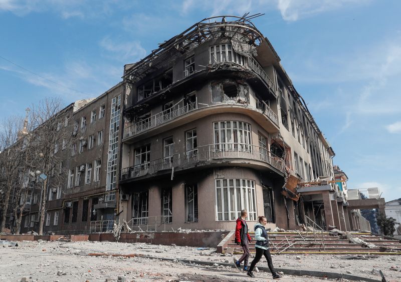 Residents walk near a building destroyed in the course of