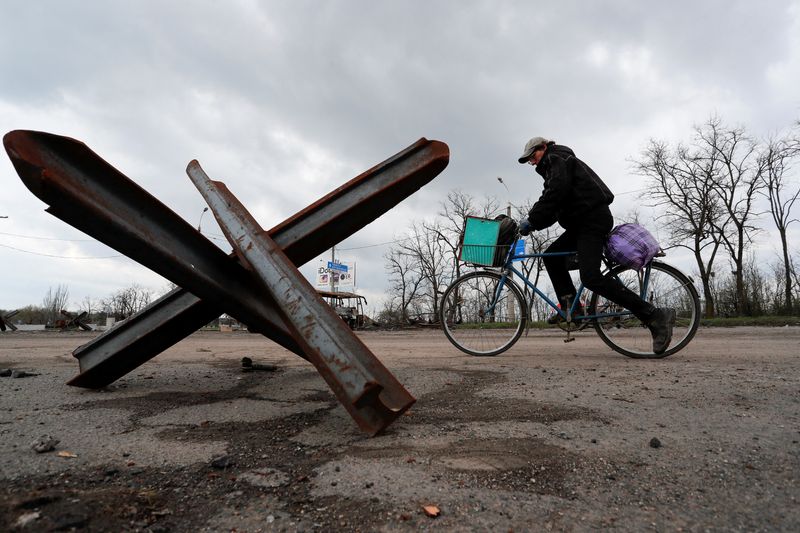 A man rides a bicycle near an anti-tank obstacle in