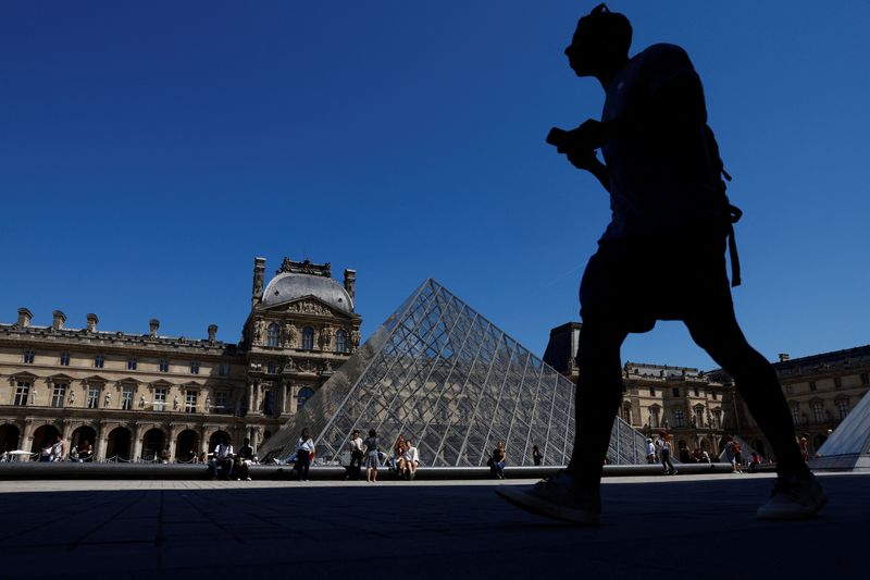 A man walks near the glass Pyramid of the Louvre