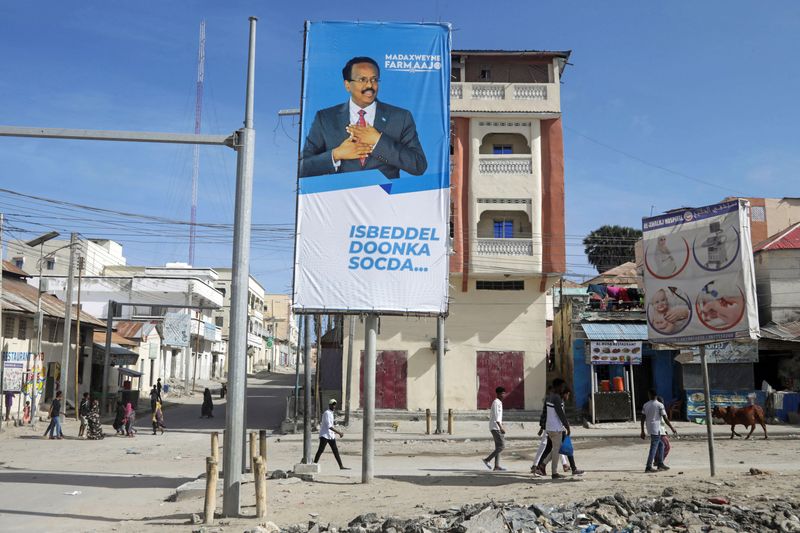People walk past an election banner of Somali President Mohamed