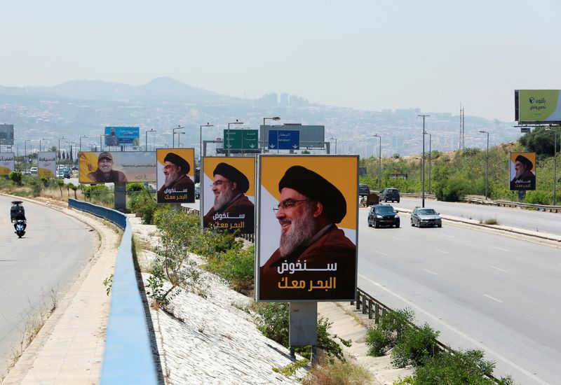 Vehicles drive past billboards depicting Lebanon’s Hezbollah leader Sayyed Hassan