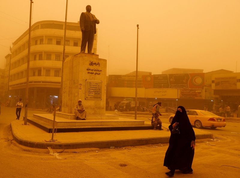 A woman walks past a statue of Iraqi poet Abdel