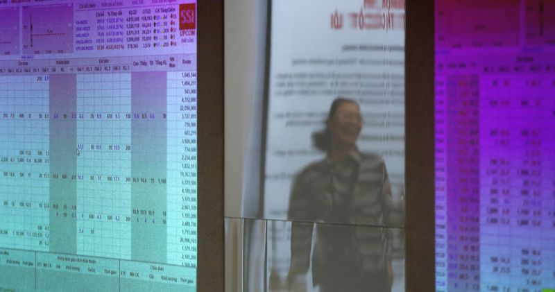 An investor is seen reflected on stock market screens at