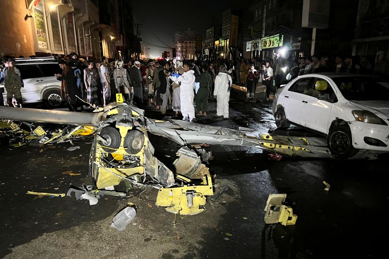 People gather around drone wreckage on street in Sanaa